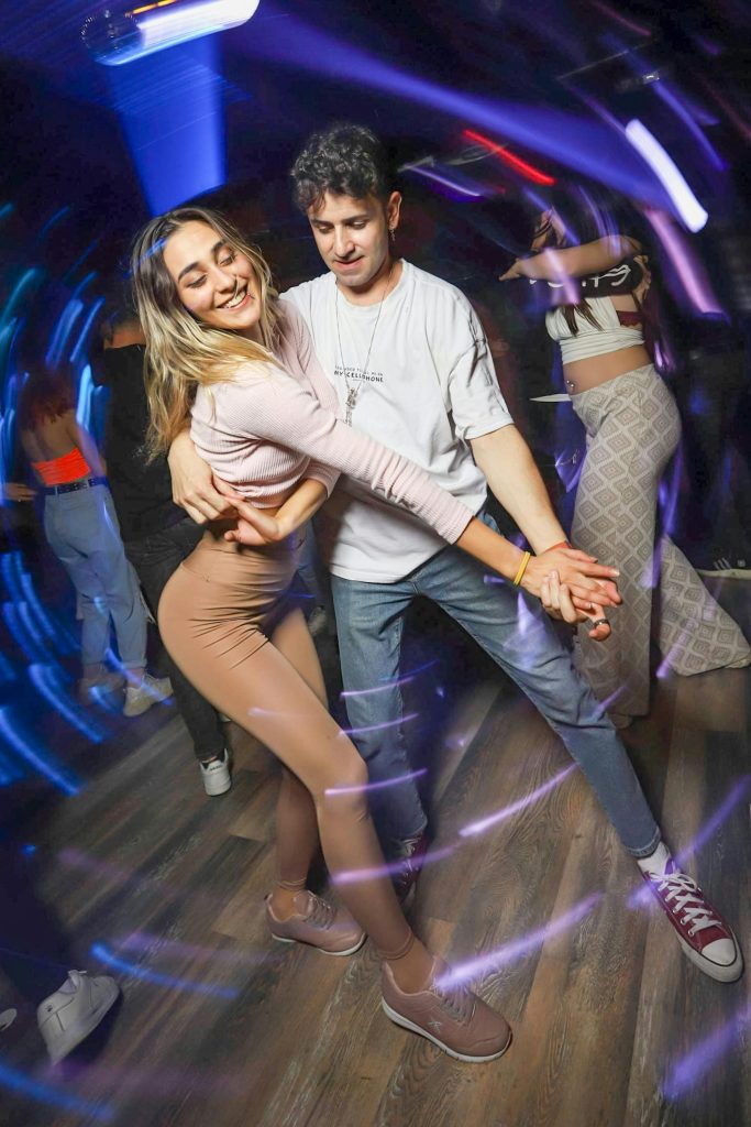 A lively couple enjoying a dance in a vibrant nightclub with dynamic lighting.